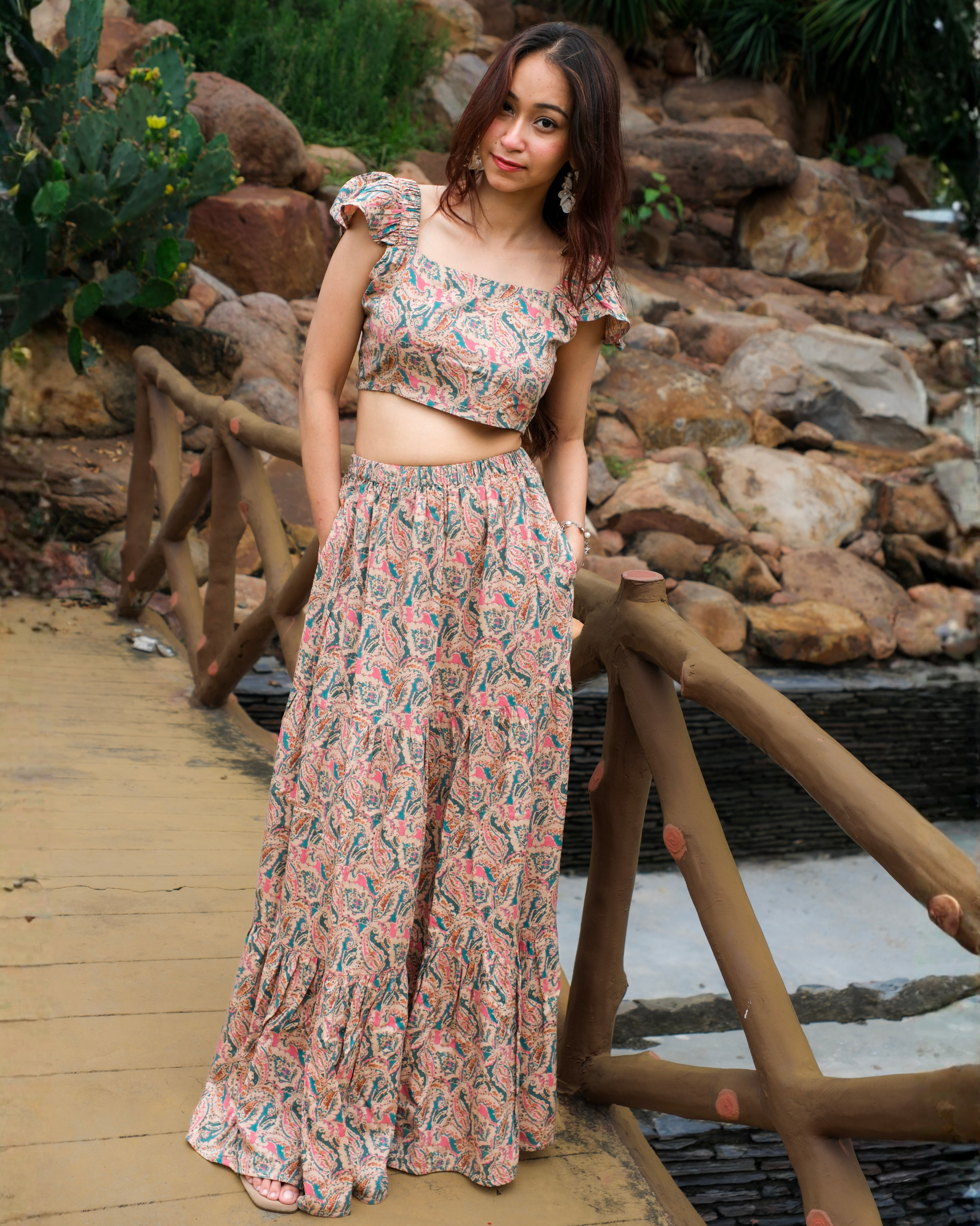 women in a beige paisley printed crop top and maxi skirt set standing on bridge. 