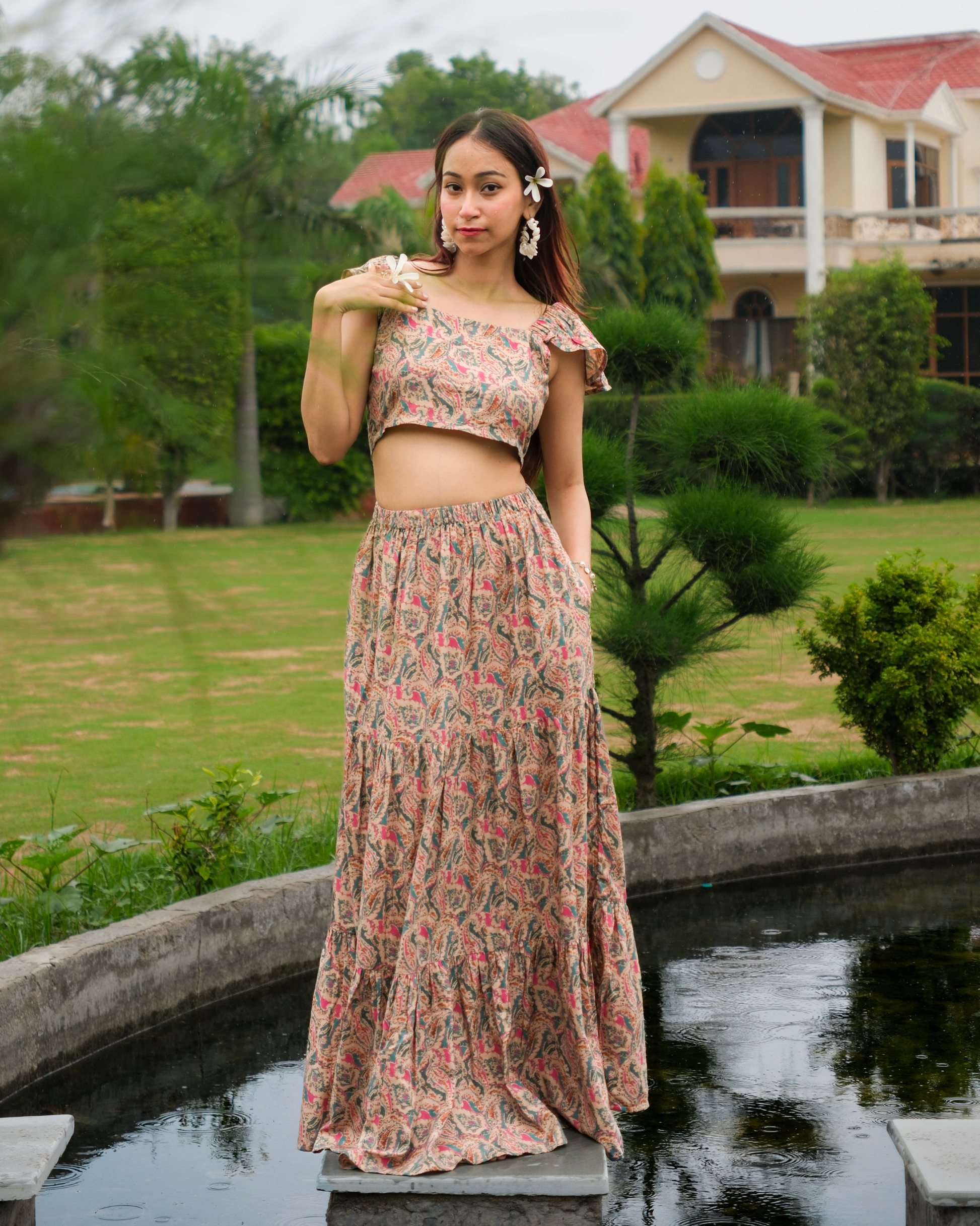 women in a beige paisley printed crop top and maxi skirt set standing near a water body in summer afternoons.