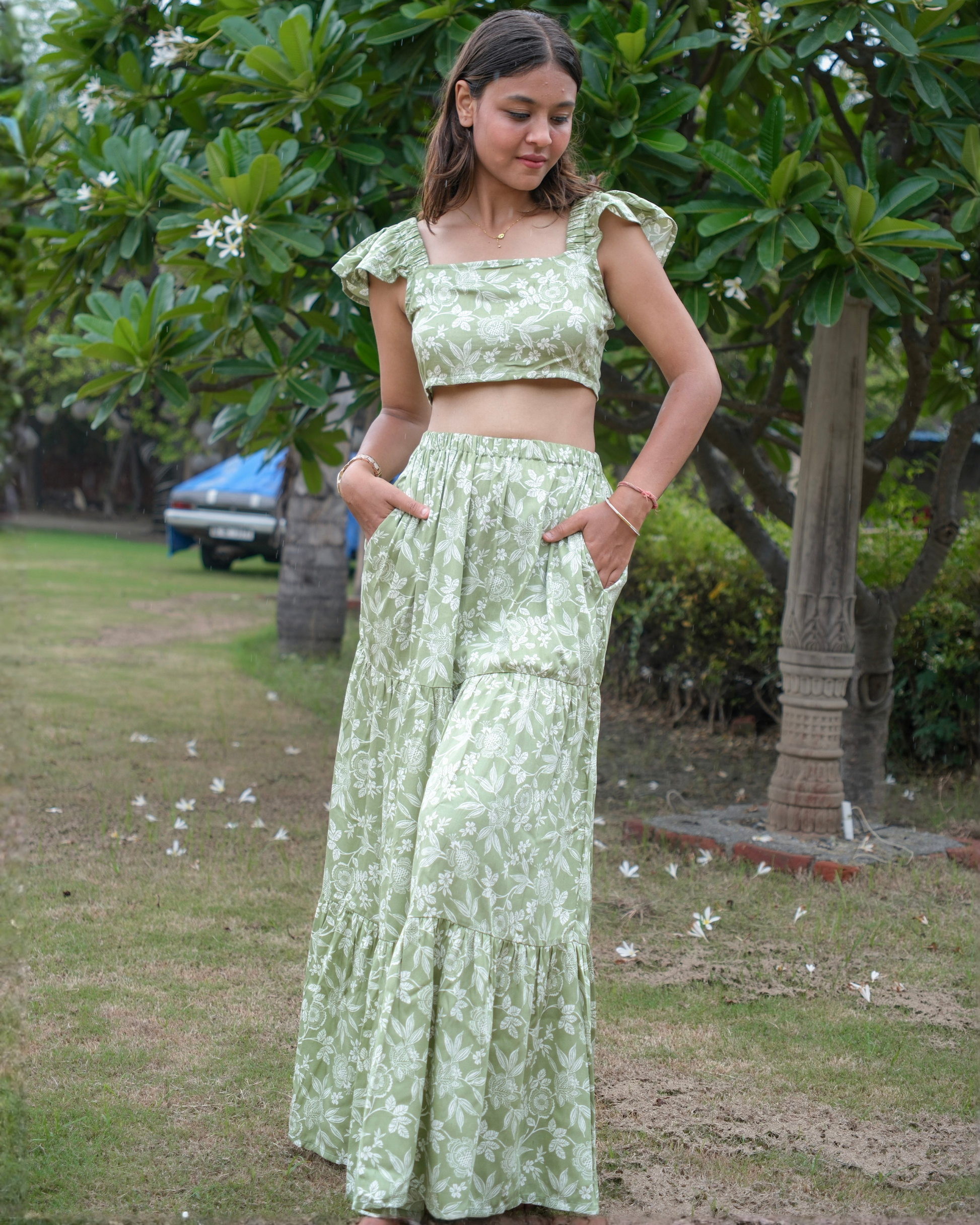 women wearing a green and white floral printed co-ord set which has pockets in the skirt standing in a park.