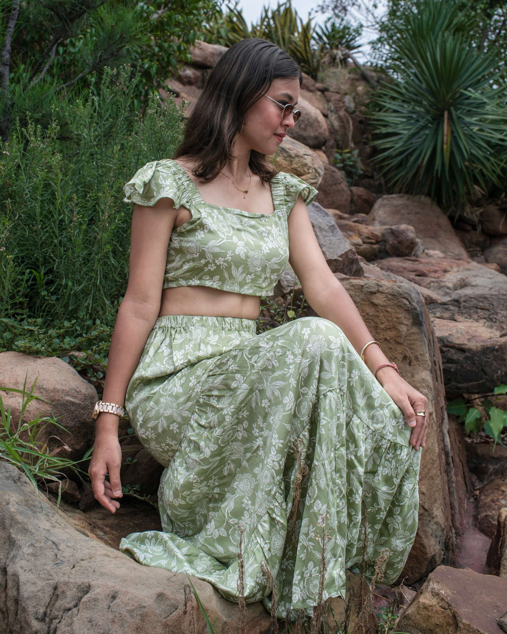 women in a green and white printed co ord set from moodora sitting on a cliff at ease.