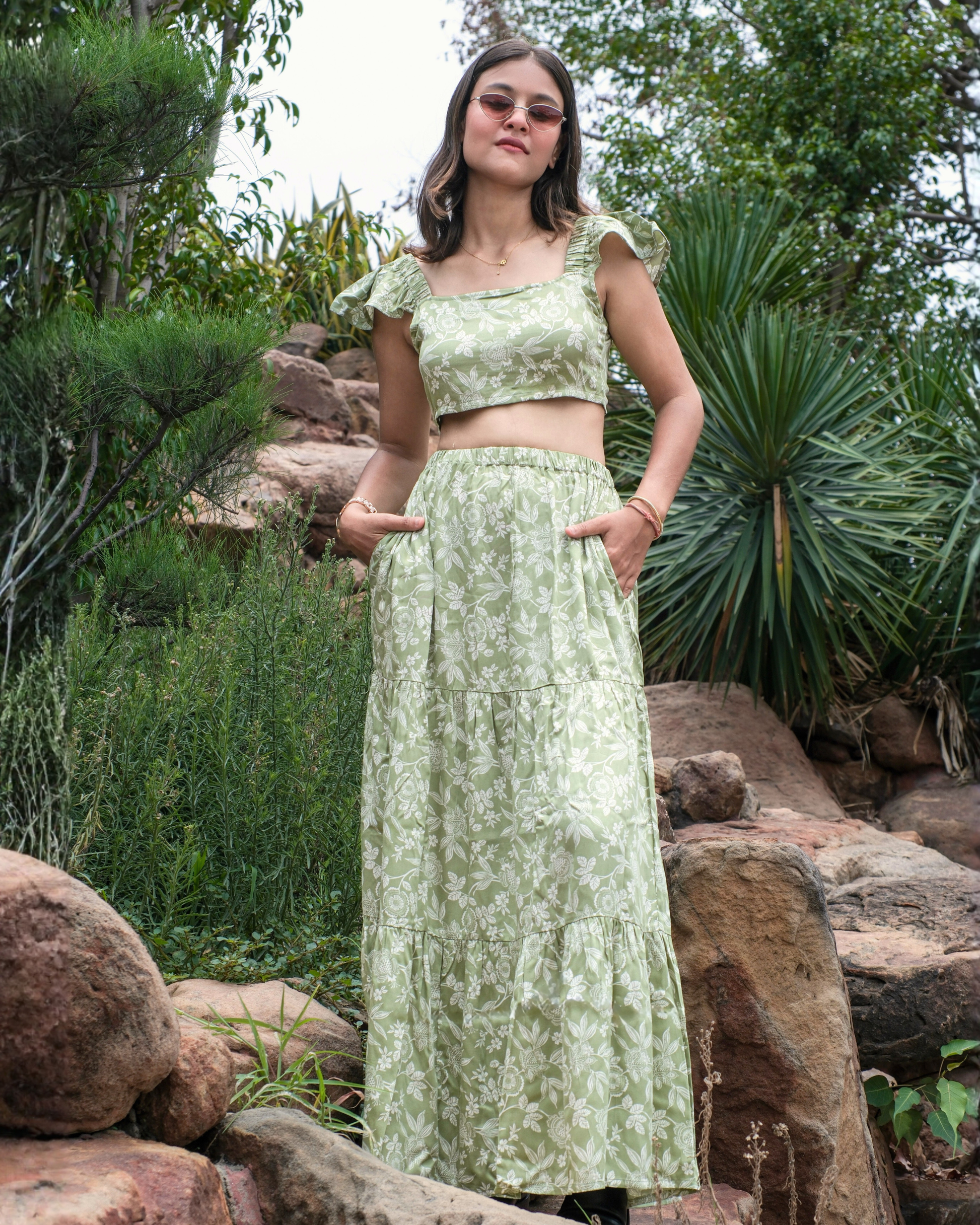 women in a green and white floral printed crop top and skirt set standing with her hands in skirt pocket.