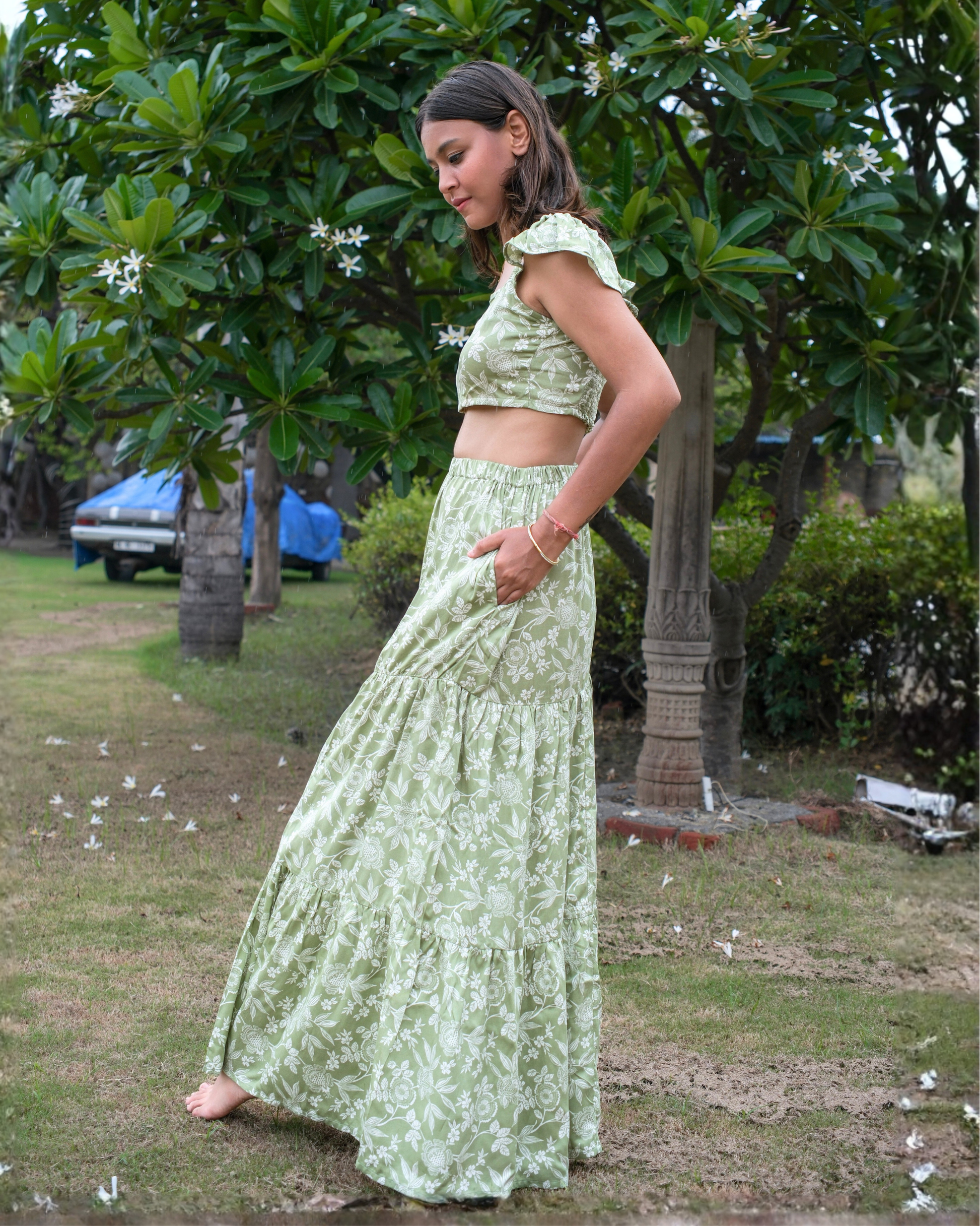 Woman in a green floral outfit standing outdoors with trees and grass in the background