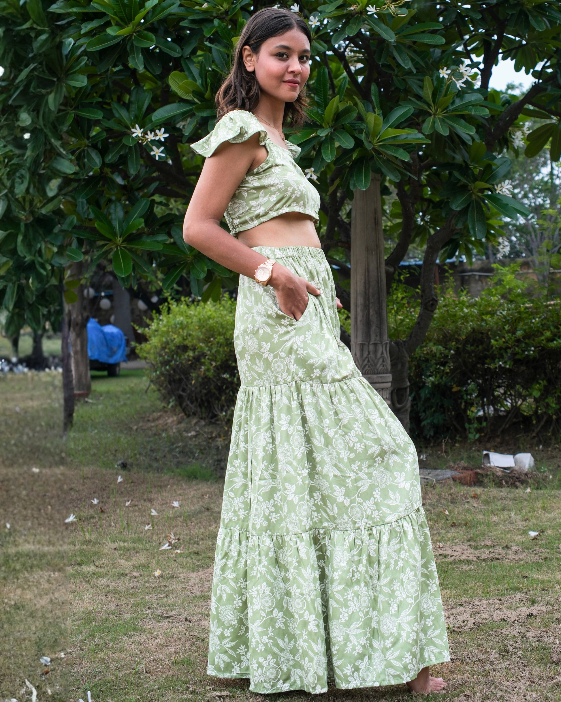 Woman in a light green floral outfit standing outdoors with greenery in the background