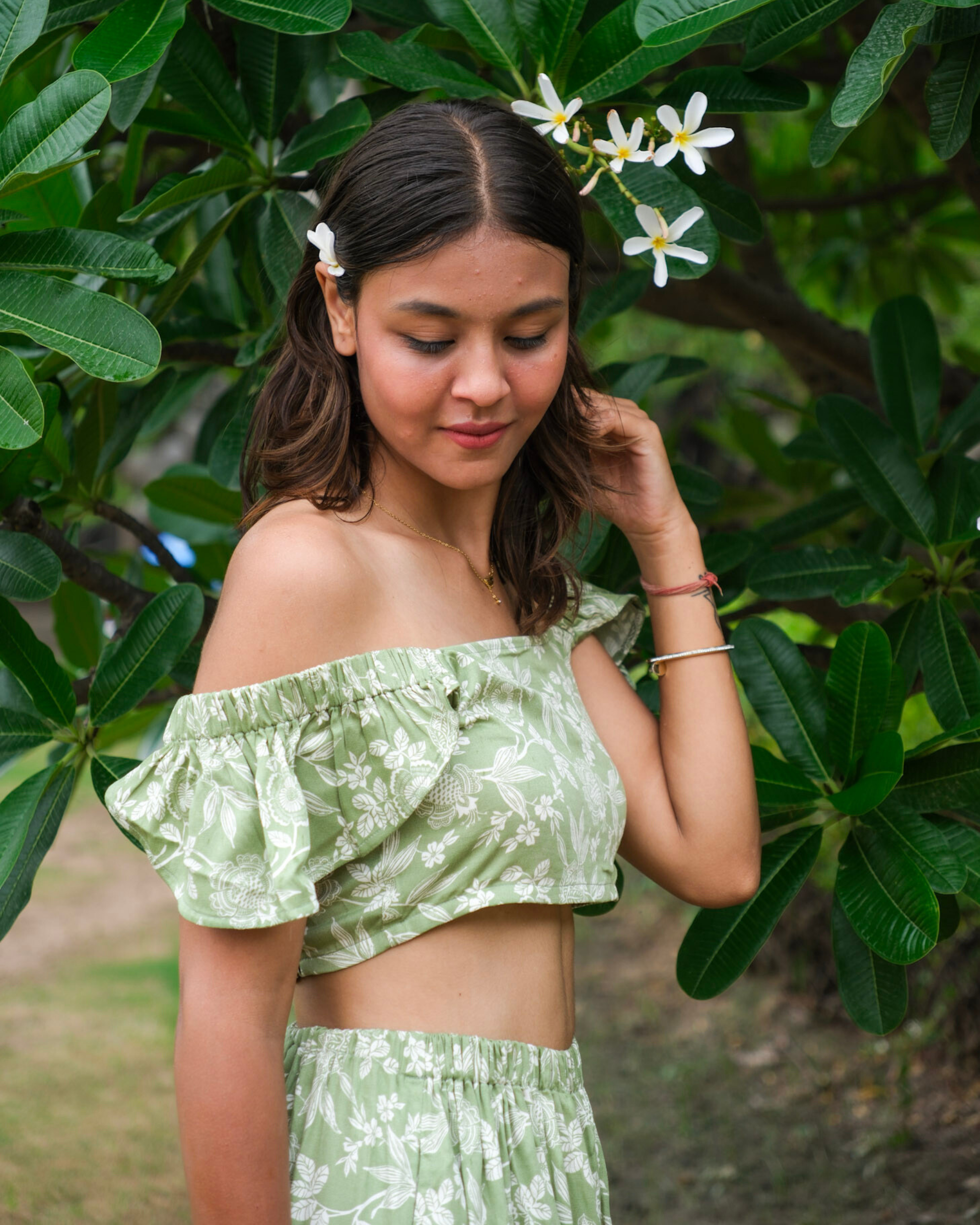 Woman wearing a green floral printed top and skirt in a natural setting with greenery.