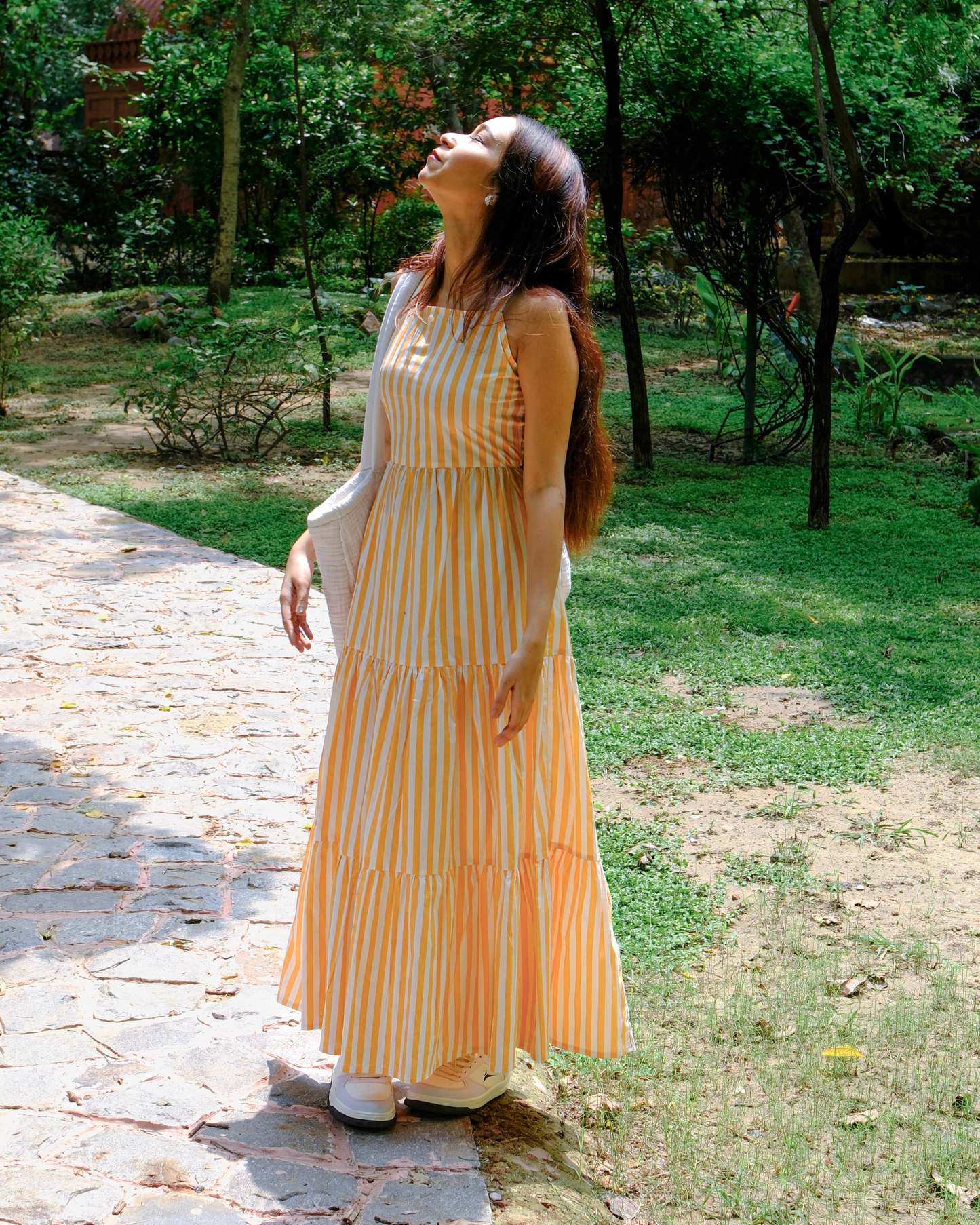 women in a white and orange stripe dress made from pure cotton by moodora standing a sunlit afternoons of summers and enjoying her time.